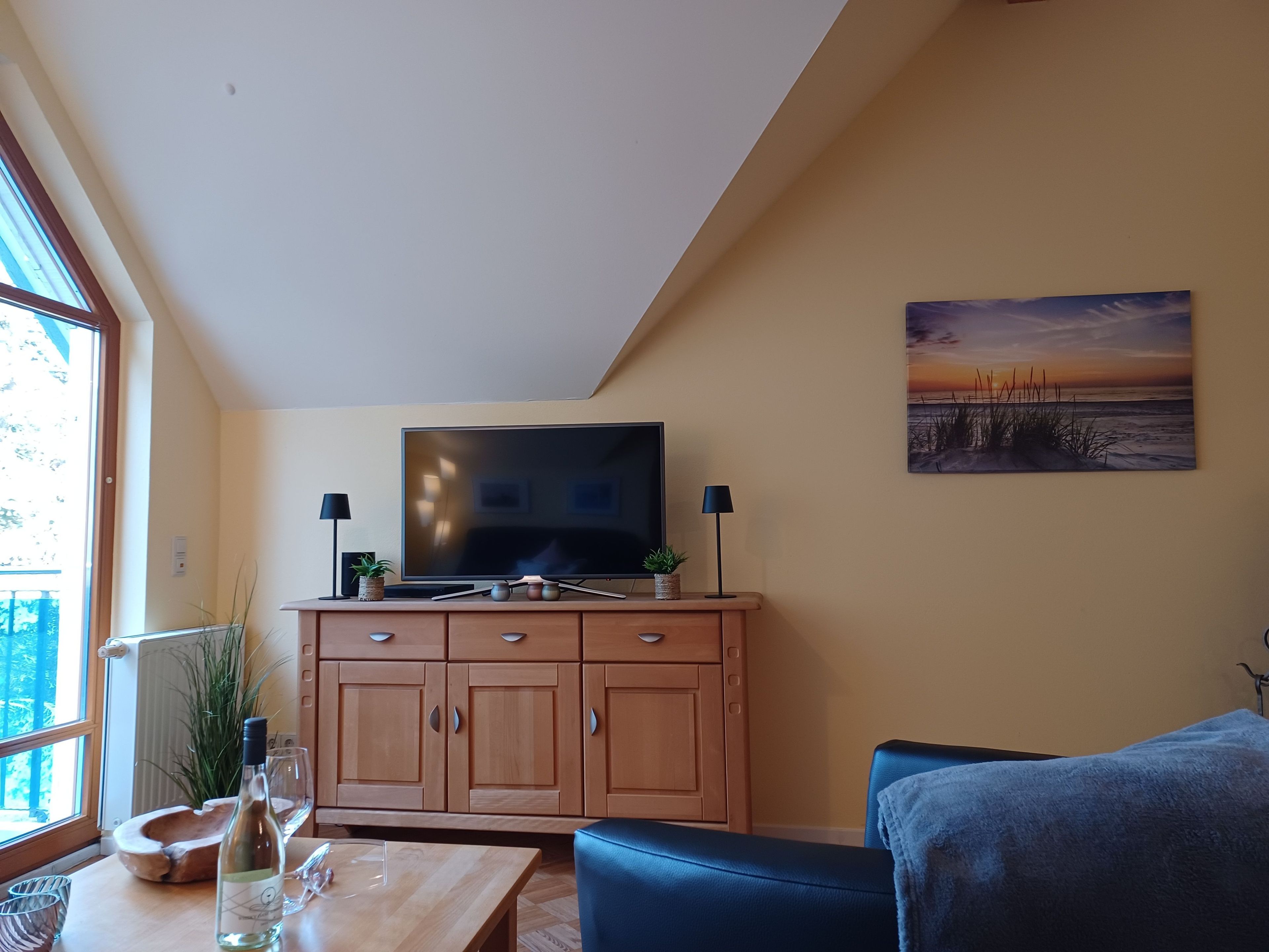 A living room with a TV, wooden cabinets, a sofa, a table with a bottle and glasses, and a painting on the wall.