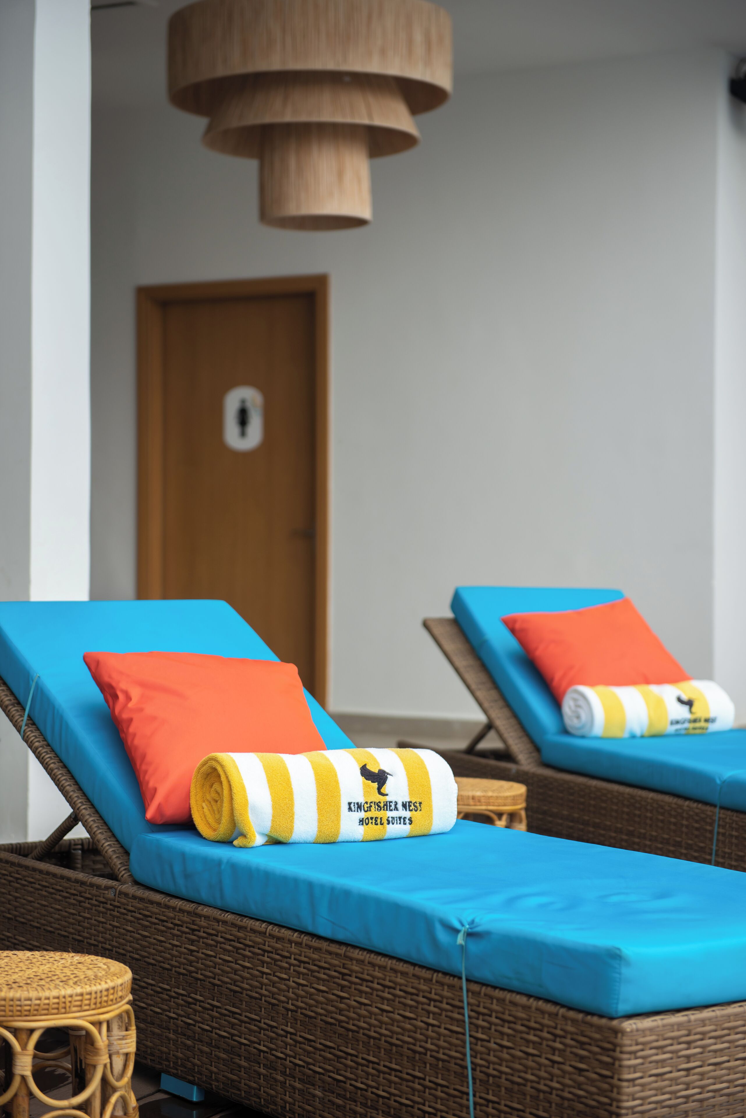 Zwei Lounge-Stühle mit blauen Kissen und orangefarbenen Zierkissen, ein Korbstuhl und ein kleiner runder Tisch.