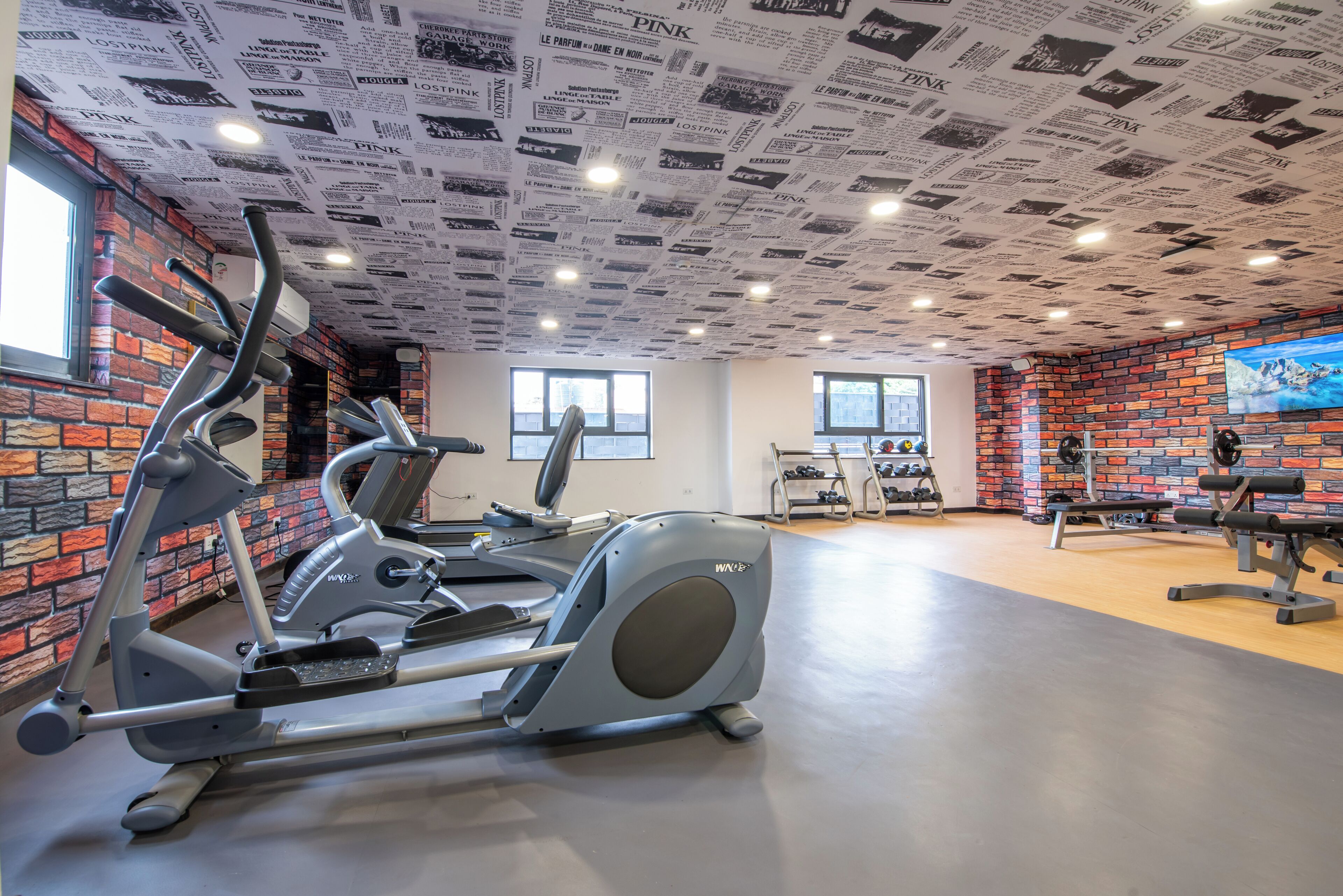 A gym with brick walls, a ceiling covered in newspaper clippings, and various exercise equipment.