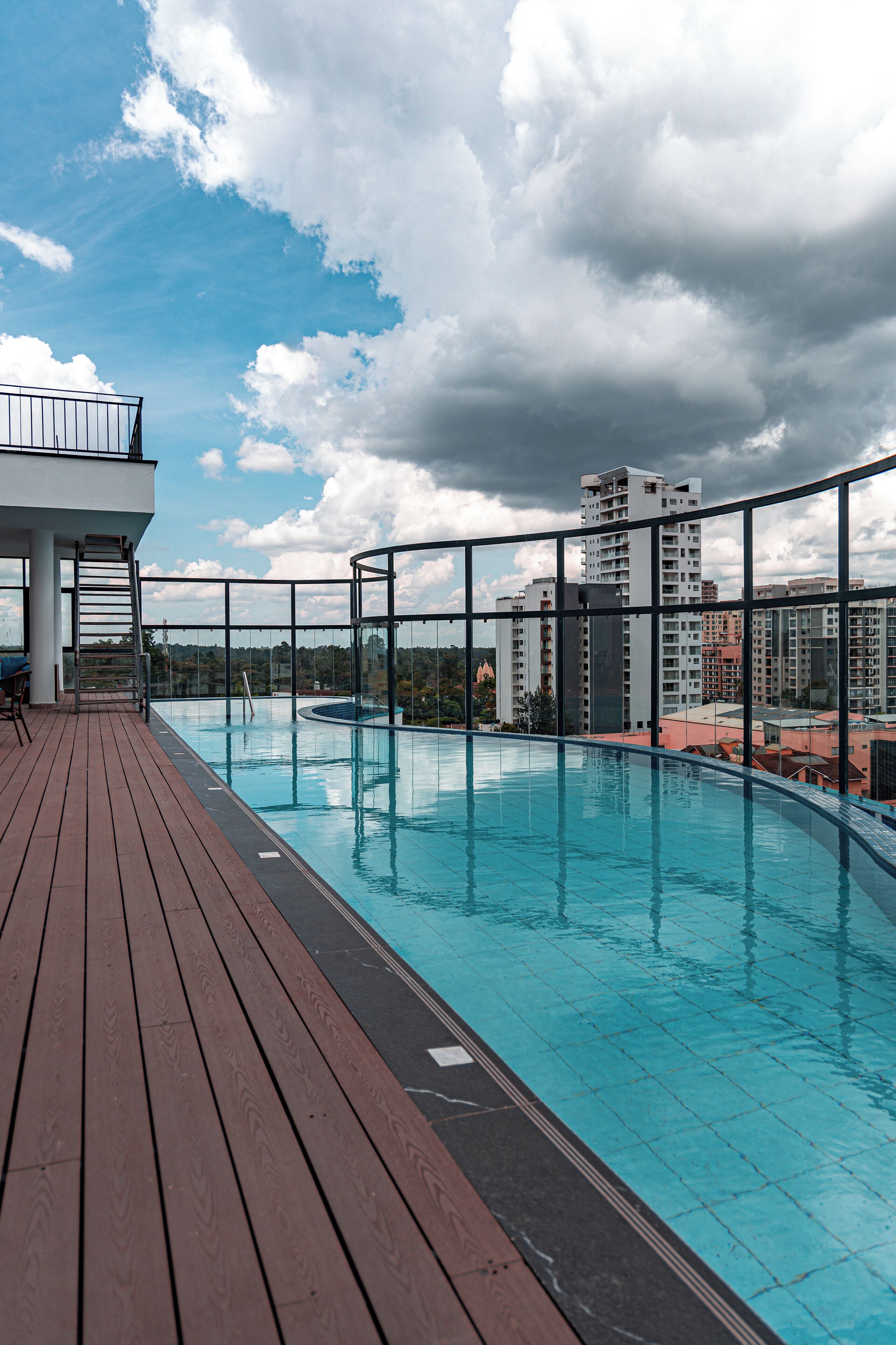 A rooftop swimming pool with a wooden deck and a view of surrounding buildings.
