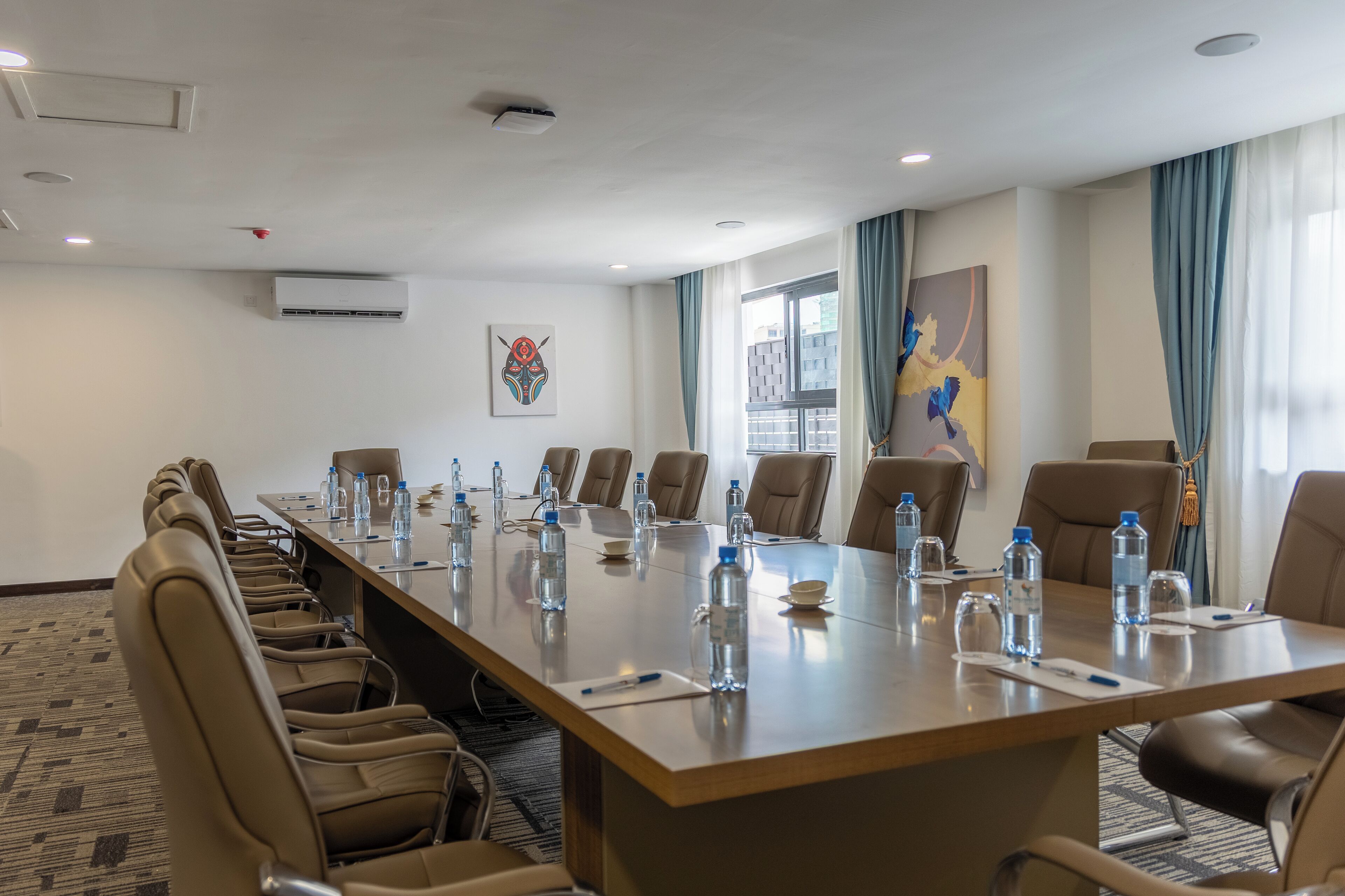 A conference room with a long table, chairs, water bottles, and a painting on the wall.