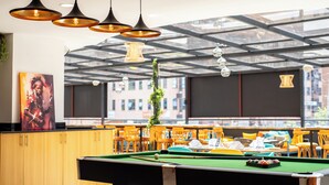A pool table with billiard balls, a green felt surface, and a cue stick. There are multiple chairs and tables in the background, and the room has a modern design with pendant lighting. - Kingfisher Nest Hotel Suites-Westlands, Near Sarit Center (Nairobi)