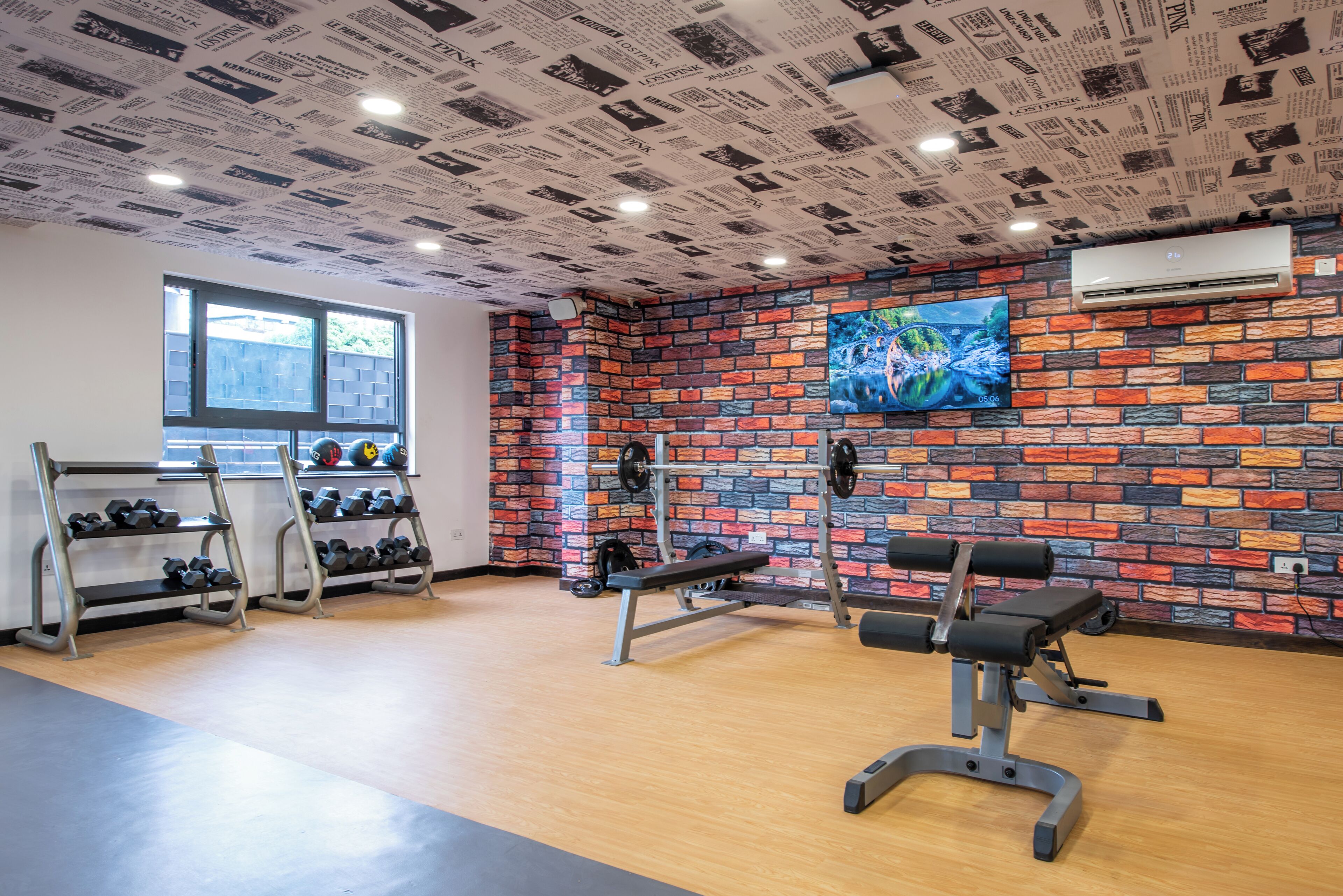 Un gimnasio con pared de ladrillo, televisión y mancuernas en estantes.