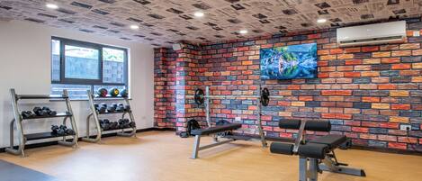 Ein Fitnessraum mit Backsteinwand, Fernseher und auf Hantelständer gestellten Gewichten.