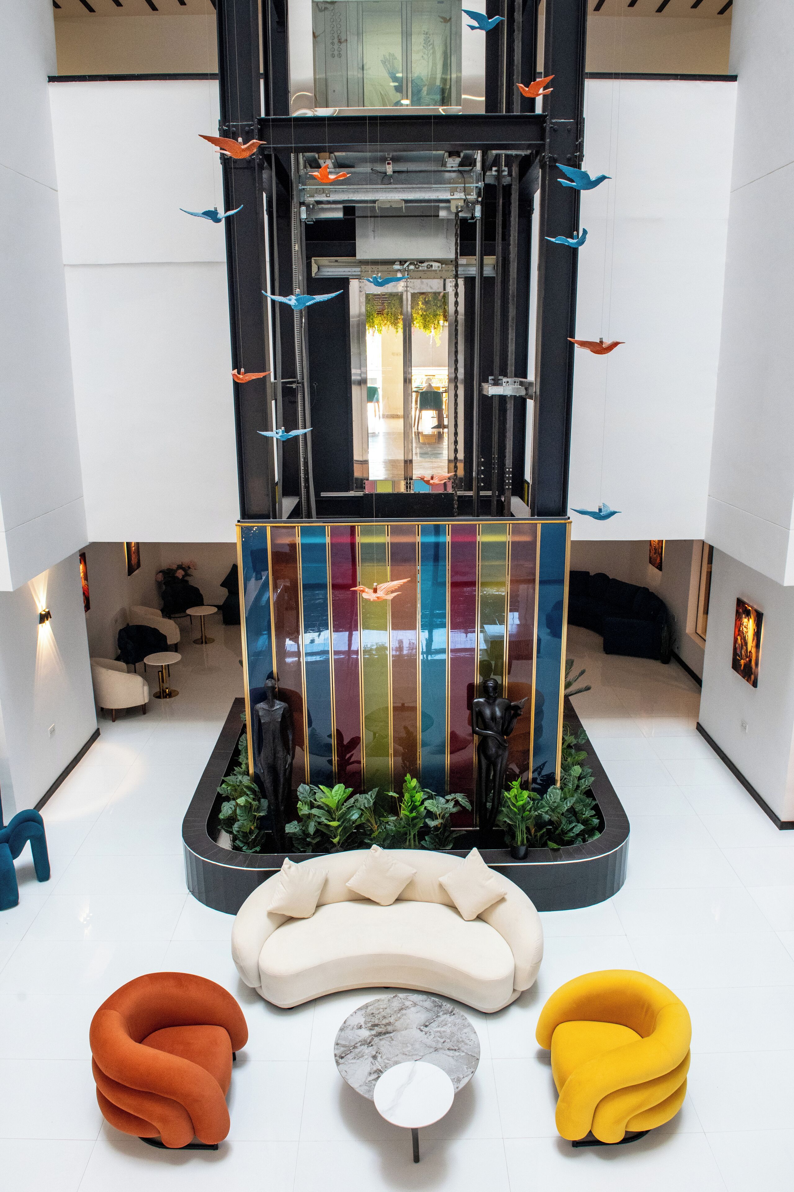 Un vestíbul modern amb una partició de vidre central, zones d'estar i escultures decoratives d'ocells.