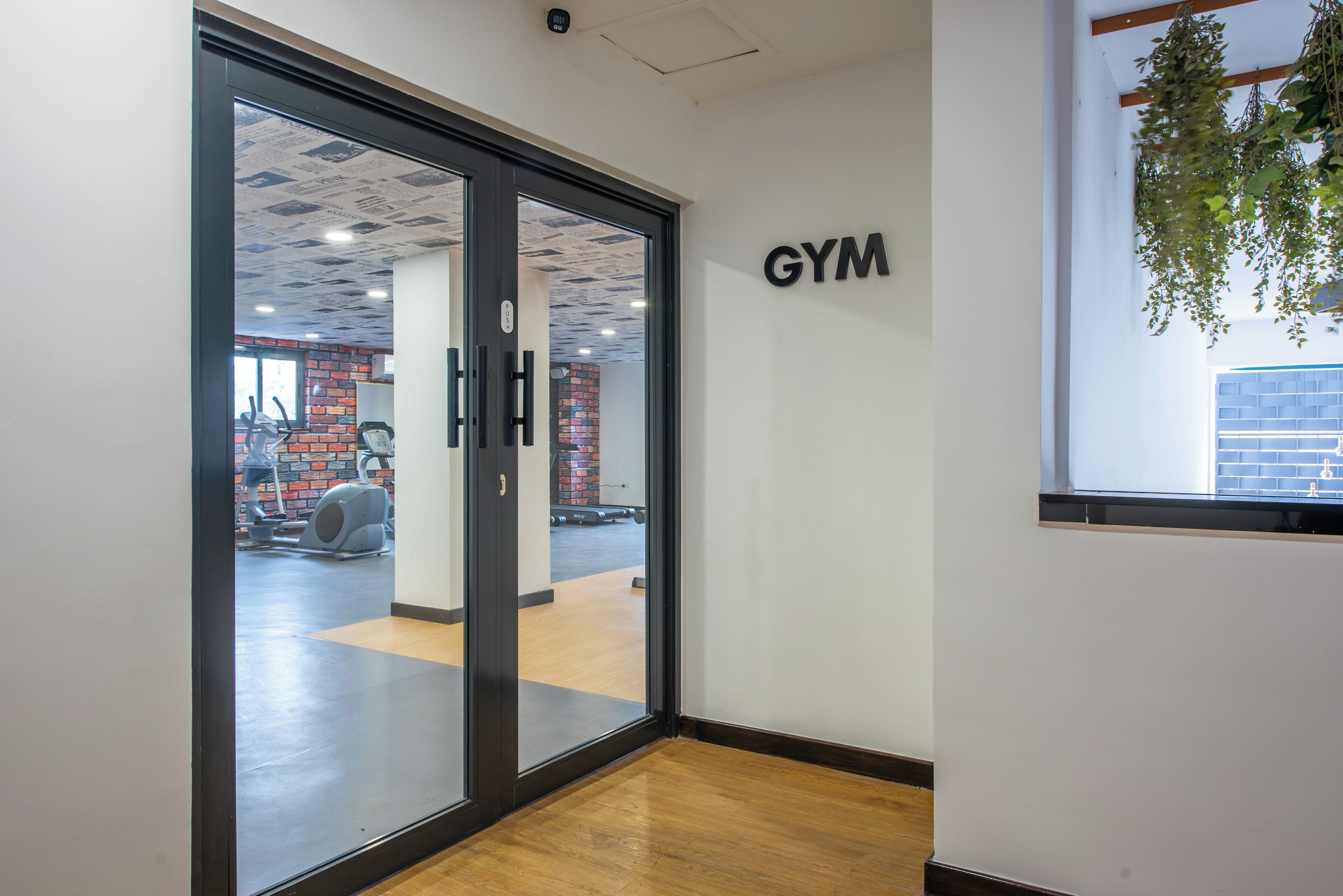A gym entrance with a glass door, a sign on the wall, and a view into the gym area with exercise equipment.