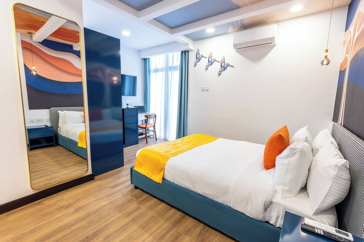 A modern hotel room with a large bed, a desk, and a mirror.