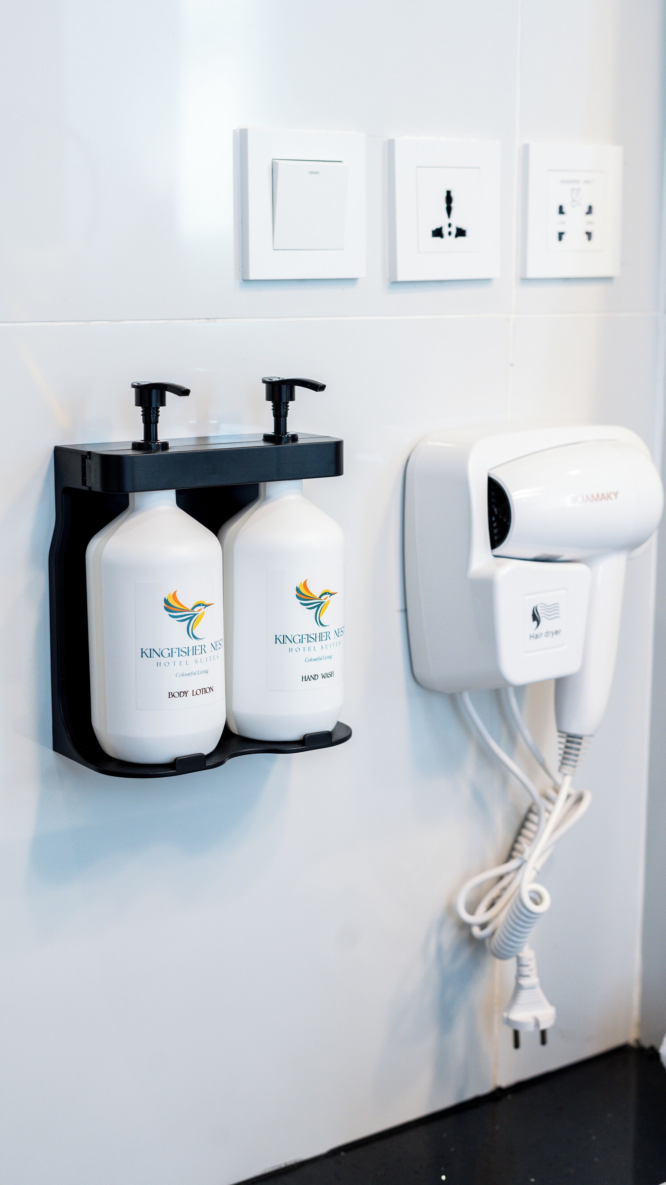 A bathroom with a hair dryer, two bottles of Kingfisher body lotion, and a power outlet.