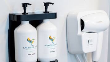A bathroom with a hair dryer, two bottles of Kingfisher body lotion, and a power outlet.