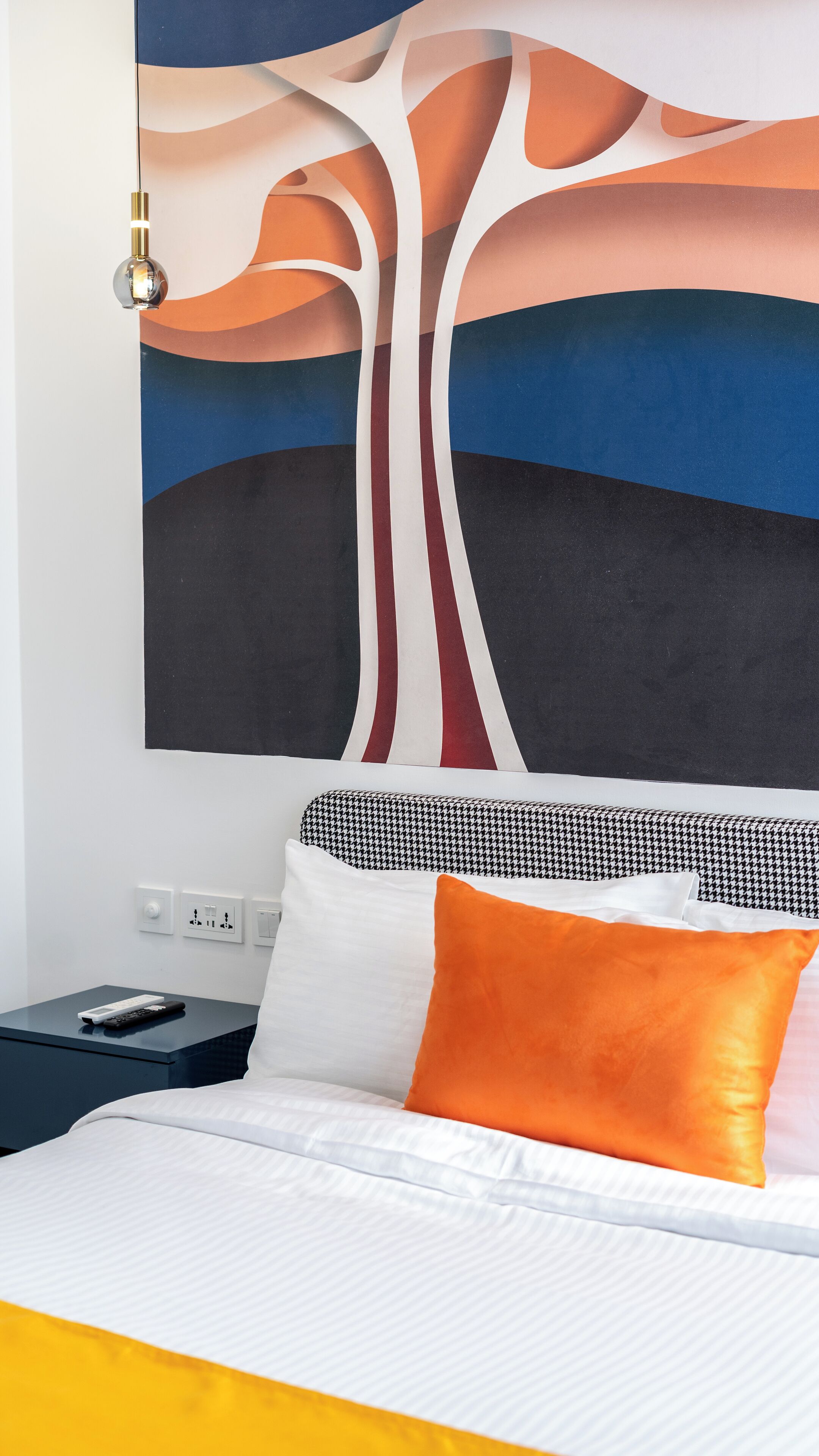 A hotel room with a bed, a nightstand, a remote control, and a wall art piece.