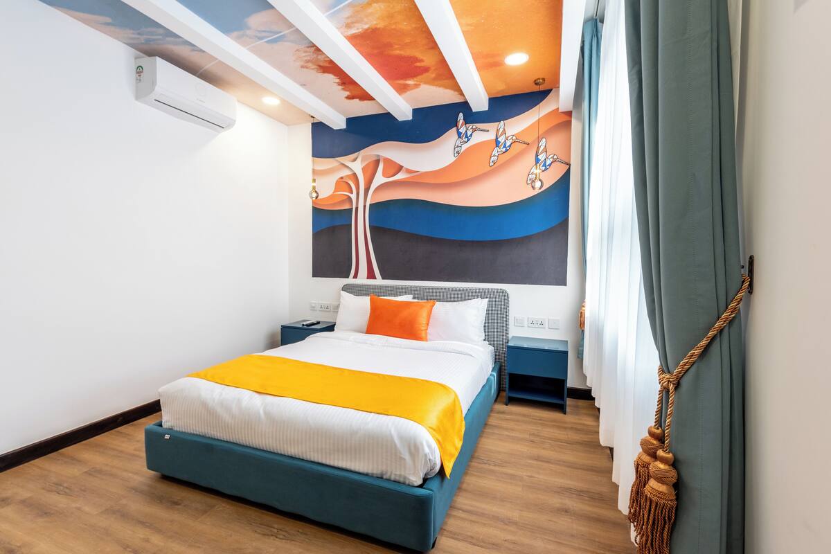 A modern hotel room with a bed, a ceiling mural, and a macrame curtain.