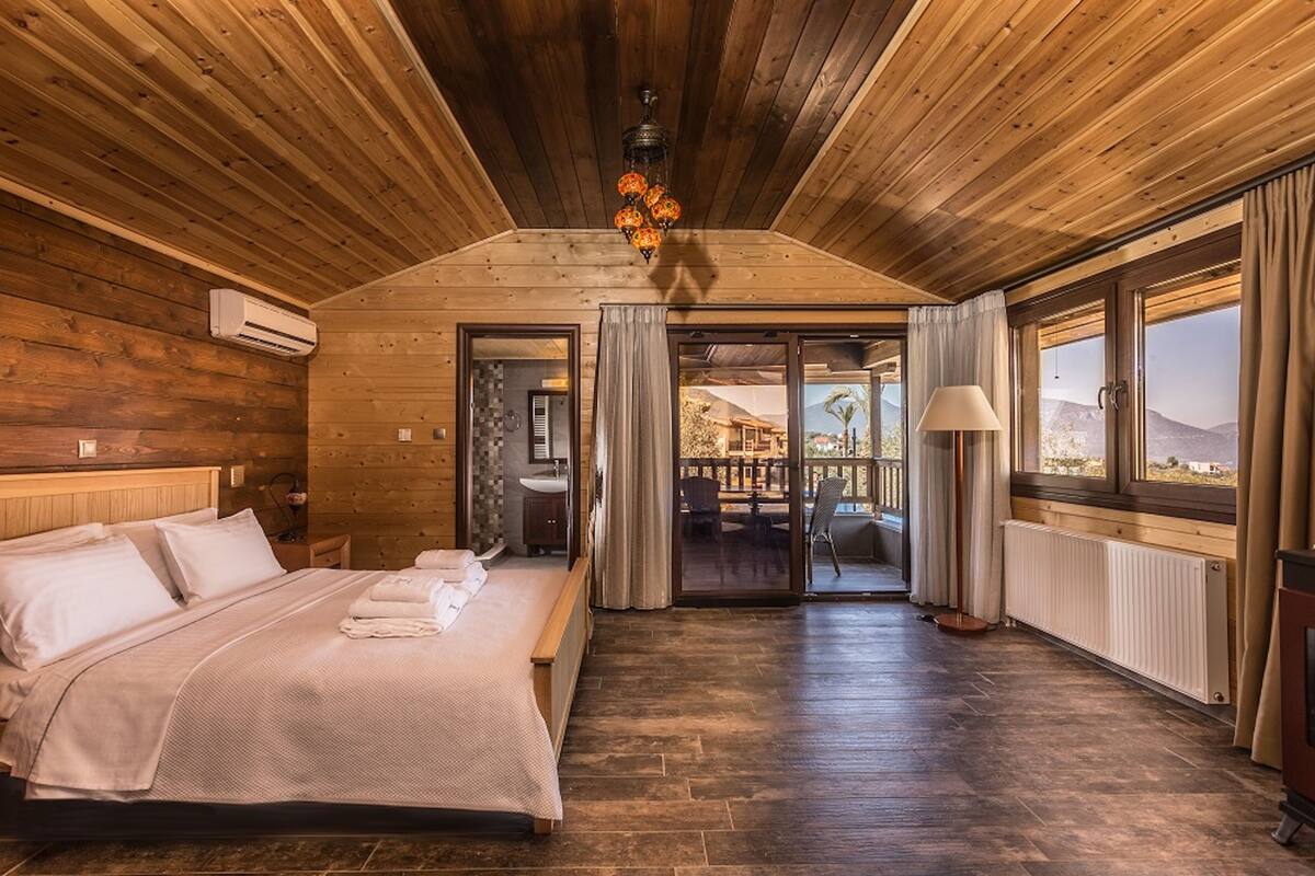 Habitación con paneles de madera, una cama, un baño y vistas a través de un ventanal.