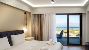 A hotel room with a large bed, a nightstand, a lamp, a view of the outdoors through a sliding door, and a ceiling light fixture. - Anthidon Estate (Chalcis)