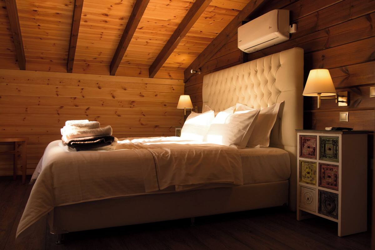Una habitación con paneles de madera, una cama, dos lámparas de noche, una mesita de noche y un aire acondicionado instalado en la pared.