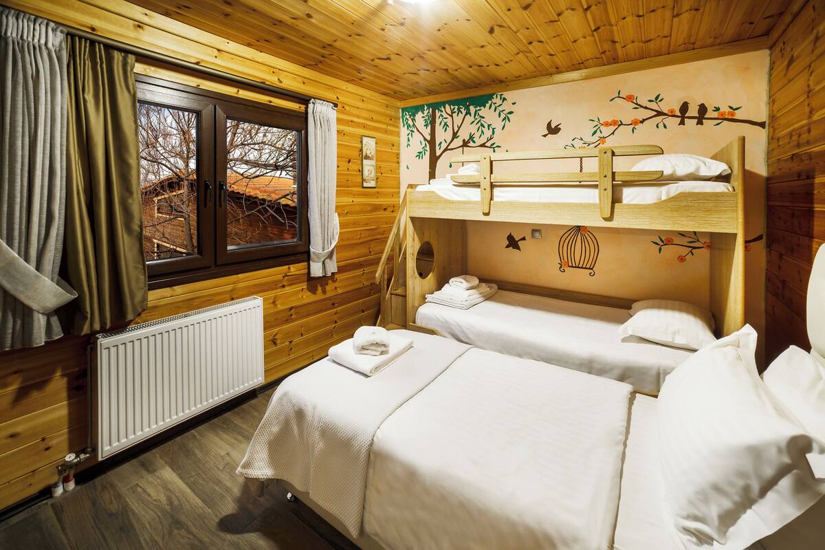 Habitación tipo cabaña de madera con dos literas, una ventana con cortinas, un radiador y un mural en la pared.