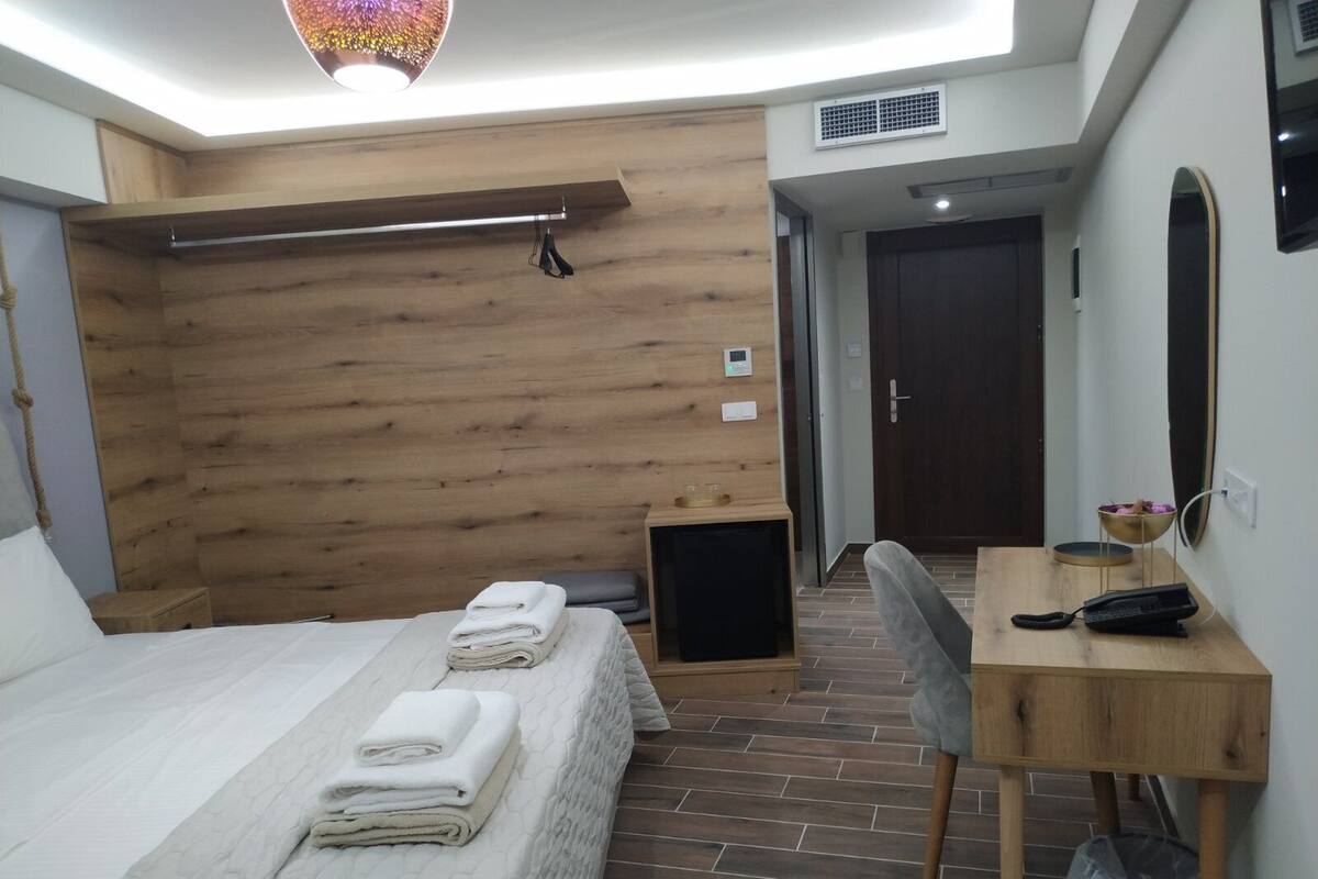 Una habitación de hotel moderna con un revestimiento de pared de madera, una cama con toallas ordenadamente dobladas, un escritorio con silla y una mesita de noche pequeña.