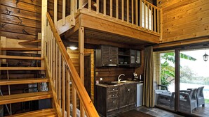 A wooden interior with a staircase leading to a balcony, a kitchen area, and a seating area with a view. - Anthidon Estate (Chalcis)