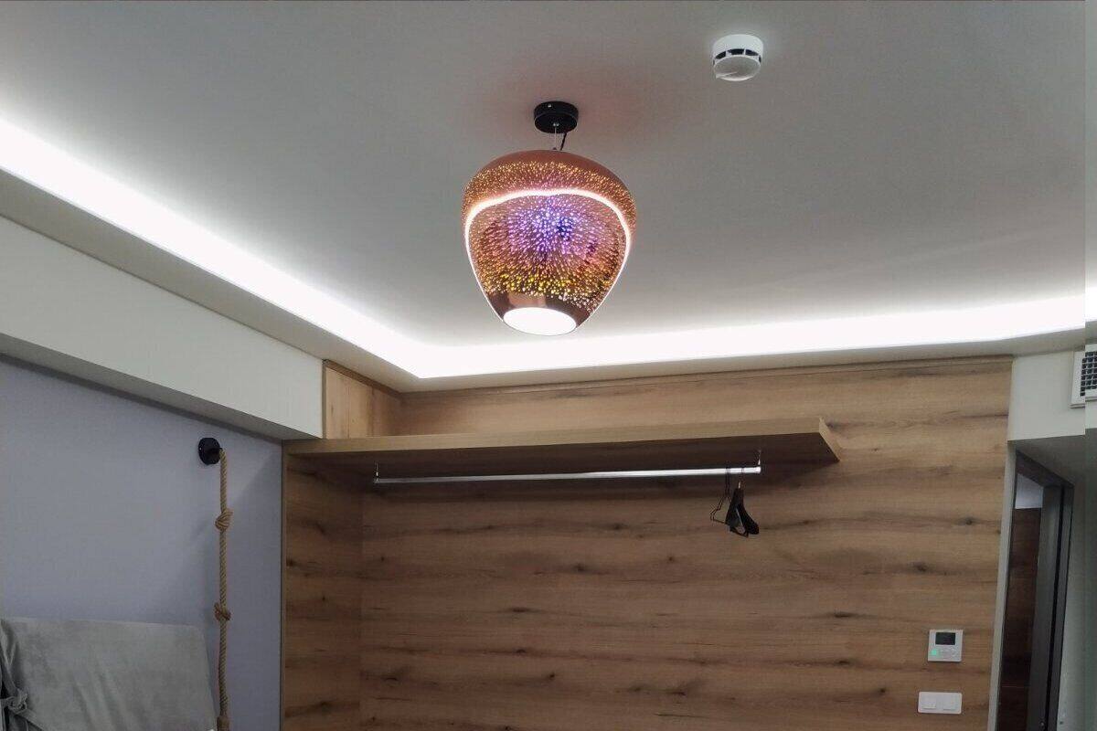 Un dormitorio moderno con una cama grande, paneles de madera en las paredes, una lámpara de techo y una mesita de noche pequeña.