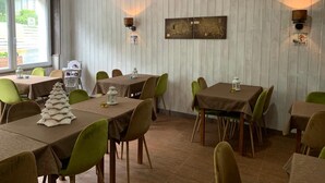 A dining area with tables and chairs, wooden panel walls, and wall-mounted lighting fixtures. - Hôtel Le Regis (Mont-Dore)
