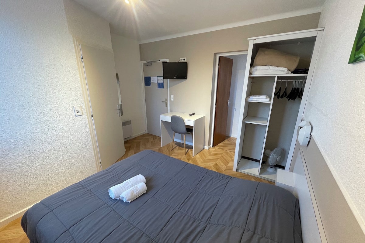 Habitación de hotel con cama, escritorio, silla, televisor y armario.