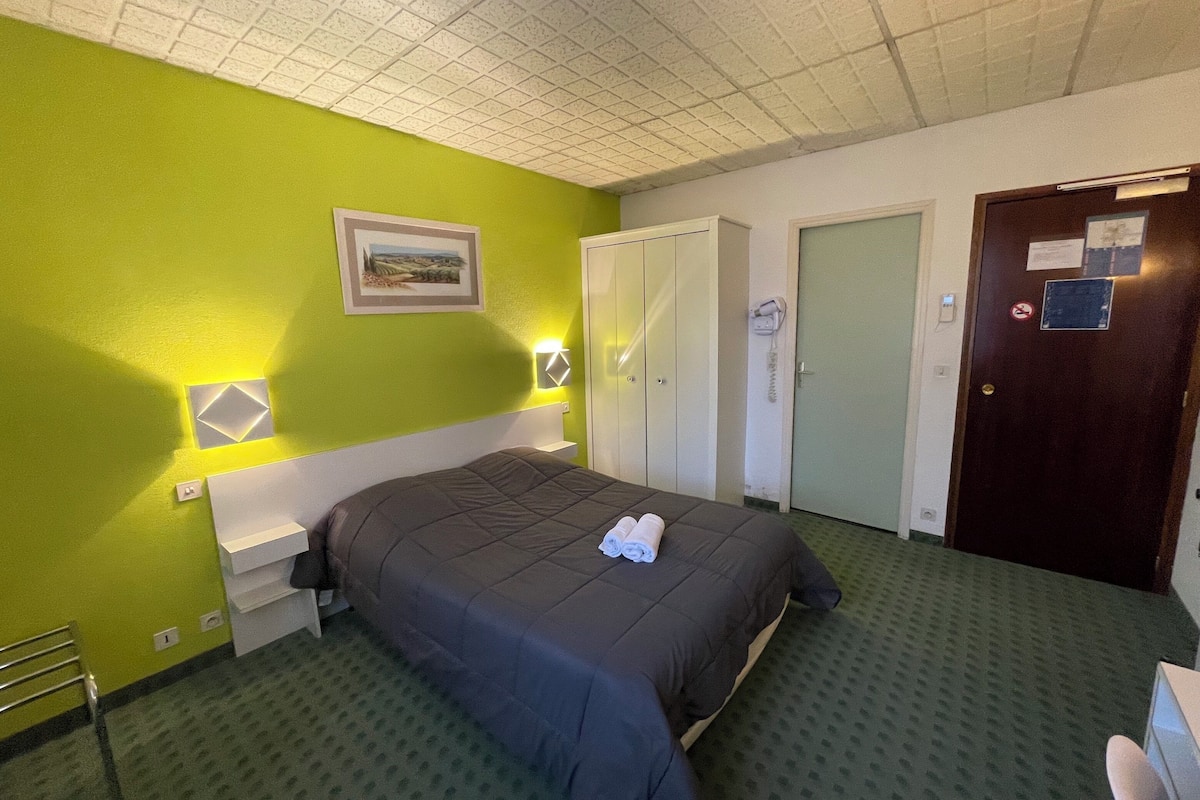 Una habitación de hotel con una cama, una pared verde, un cuadro y una puerta.