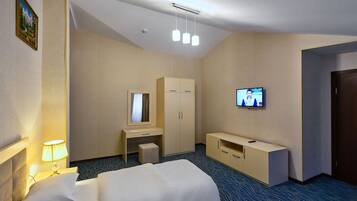 A hotel room with a bed, a desk, a wardrobe, a television, and a lamp.