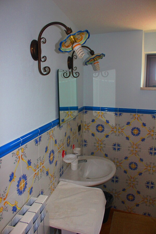 A bathroom with a white sink, a toilet, and a decorative mirror with a floral tile backsplash.