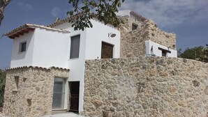 A two-story stone building with a white facade, a small balcony, and a door with a metal gate. - Casale Racalmare (Grotte)