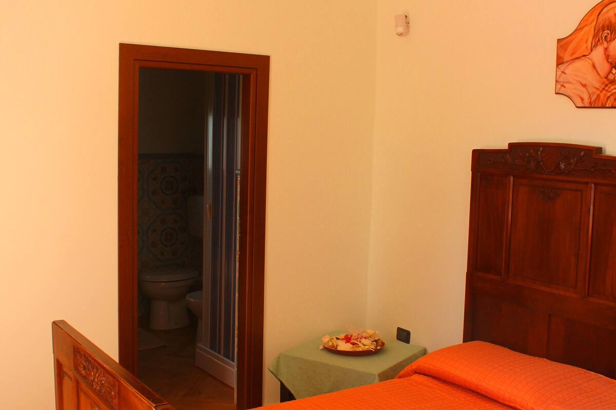 A bedroom with a wooden bed, a small table, and a door leading to a bathroom.