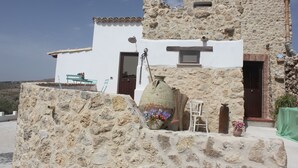 A stone building with a white exterior, a large vase with flowers, and a small table with chairs. - Casale Racalmare (Grotte)