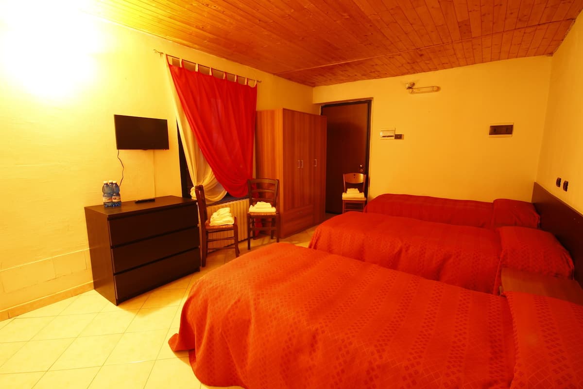 Une chambre avec deux lits, un plafond en bois, une télévision, une armoire, une chaise et un rideau rouge.