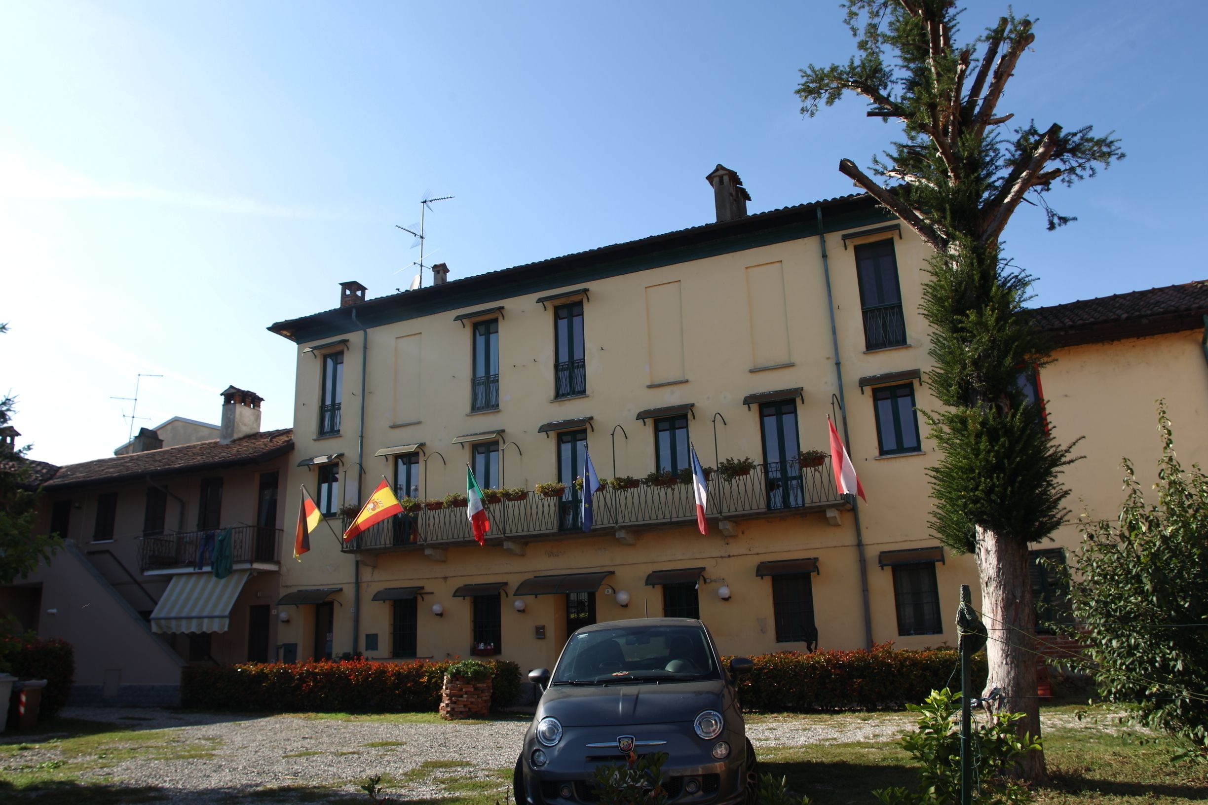 A building with multiple balconies, flags, and a parked car in front.