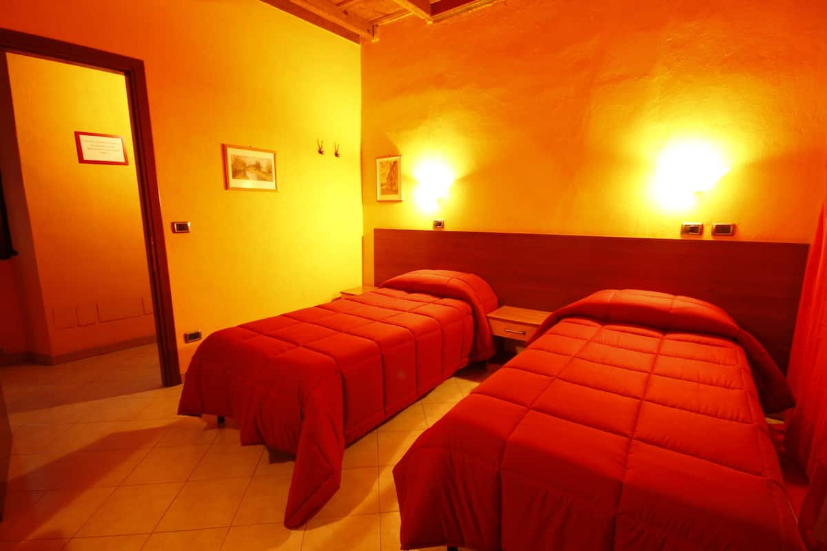 Une chambre avec deux lits, une tête de lit en bois, une table de chevet et une lampe fixée au mur.