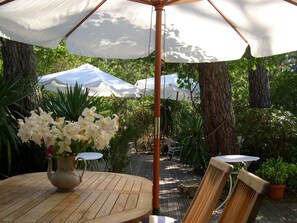Ein Holztisch mit einer Blumenvase, zwei Stühlen und einem großen Sonnenschirm, der Schatten spendet.