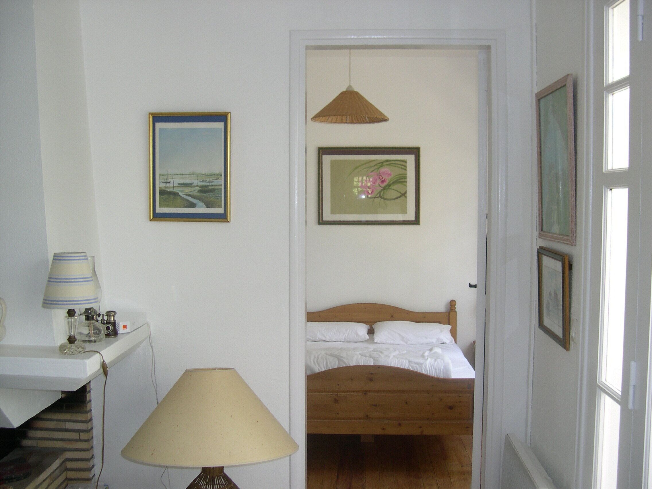 A bedroom with a wooden bed, a bedside table with a lamp, and two framed pictures on the wall.