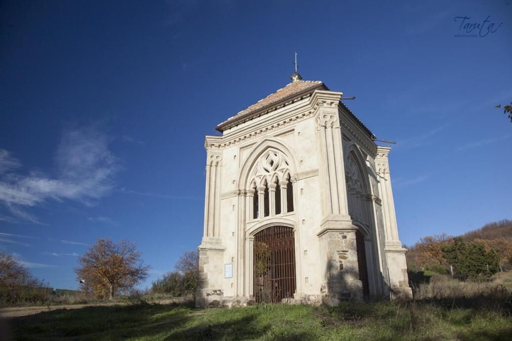 A historic stone structure with a pointed arch and a large wooden door, surrounded by grass and trees.