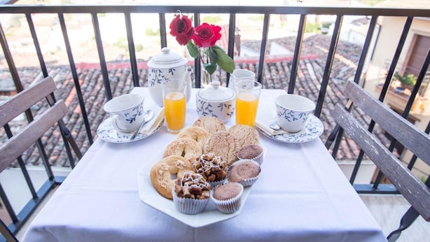 Una mesa en un balcón con desayuno: tetera, tazas, vasos y pasteles.