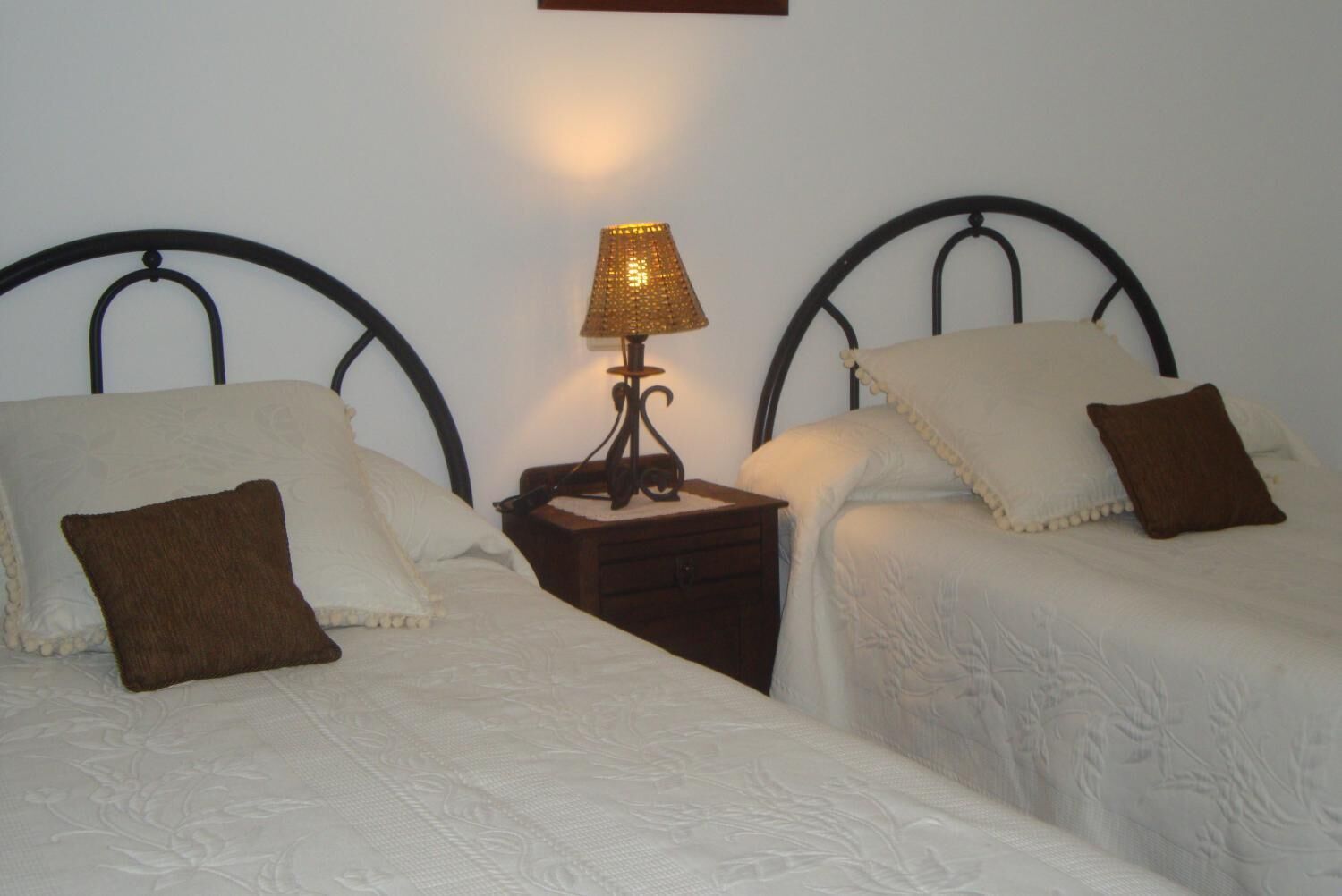 A twin room with two beds, a nightstand with a lamp, and a wall-mounted shelf.