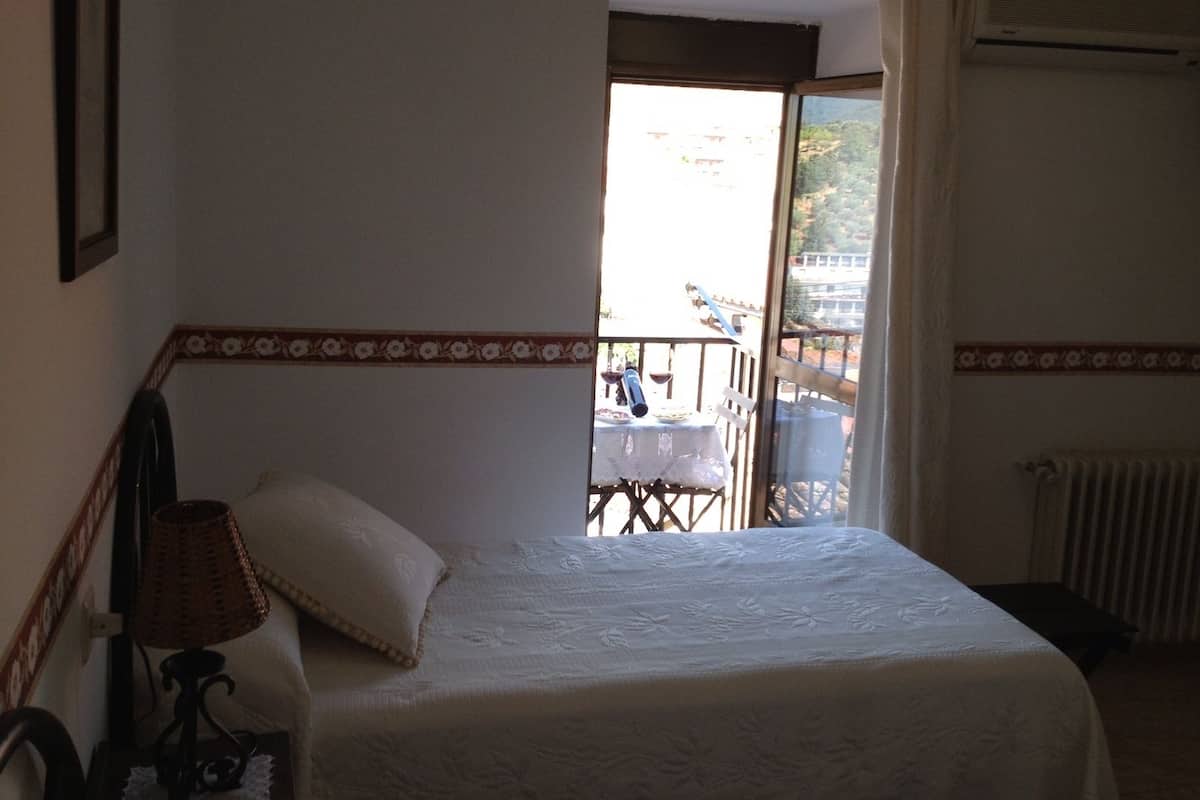 Ein Schlafzimmer mit einem Bett, einem Nachttisch, einer Lampe und Blick auf einen Balkon.