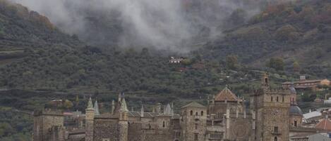 Un castillo de piedra histórico con una torre de reloj destacada, rodeado por un pueblo con arquitectura tradicional.