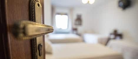 Un gros plan d’une poignée de porte en laiton avec un trou de serrure, donnant sur une pièce où se trouvent un lit et une fenêtre.