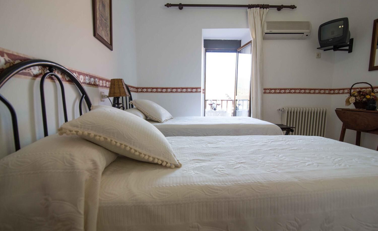 Ein Hotelzimmer mit zwei Betten, einem kleinen Tisch, einem Sessel, einer Klimaanlage, einem Fernseher und einem Fenster mit Blick.