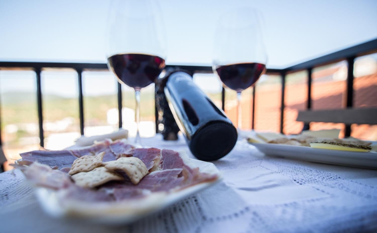 A table with a bottle, glasses, and food on a balcony.
