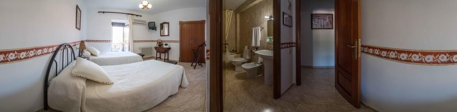 Una habitación de hotel con dos camas, un baño con lavamanos e inodoro, y un pasillo que conduce a otra habitación.