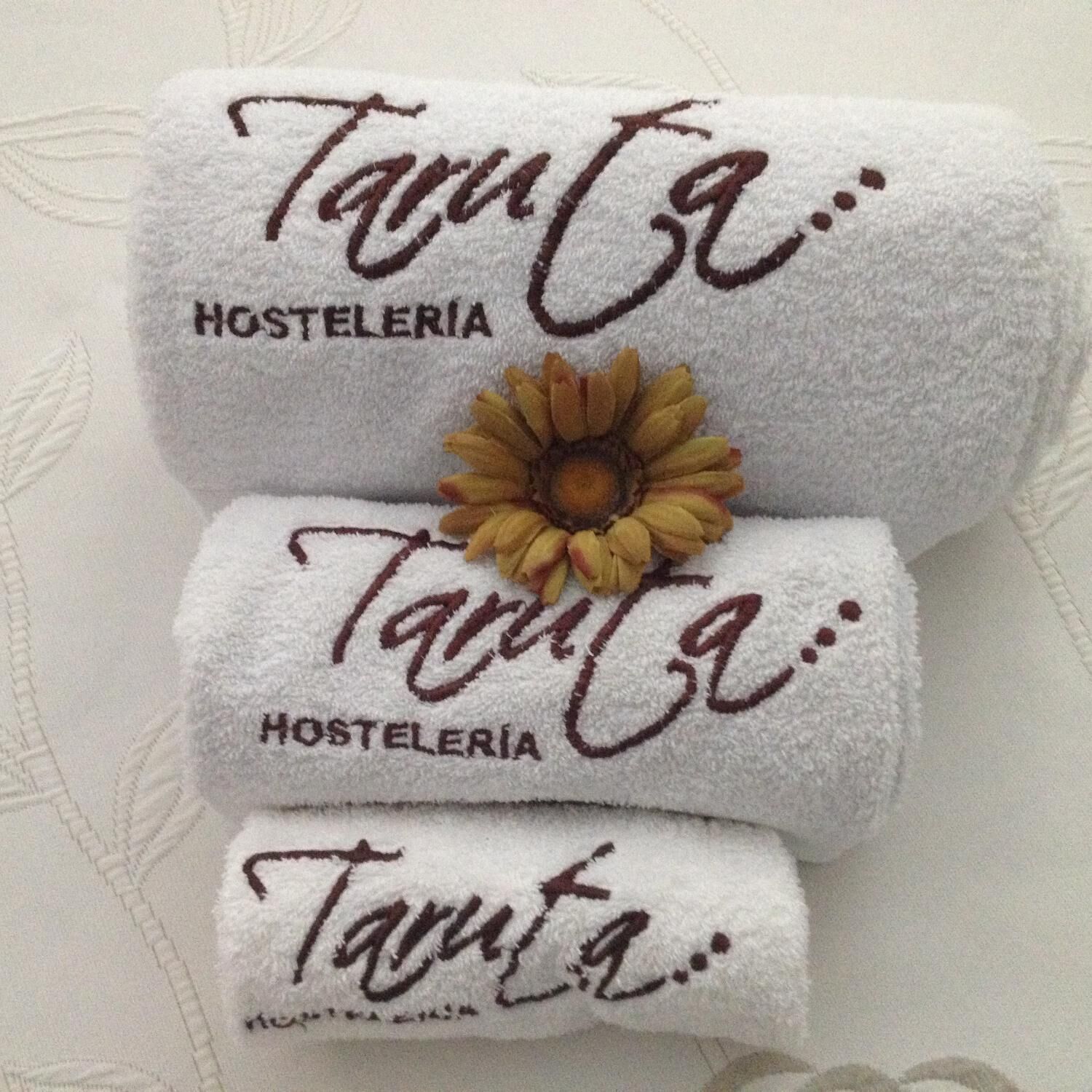 Tres toallas dobladas con bordado de texto y un adorno de girasol.