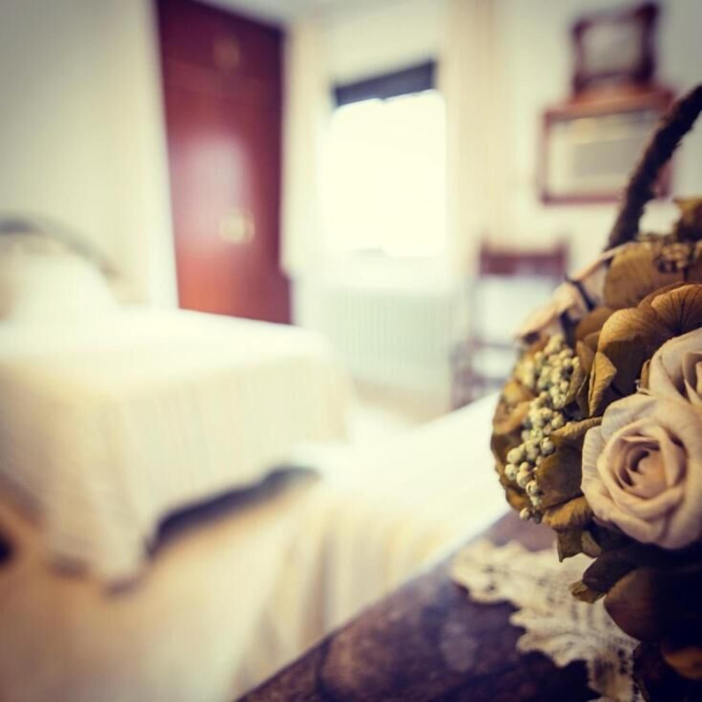 Habitación de hotel con cama, ventana y un arreglo decorativo de flores y hojas.