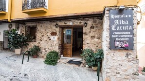 Un edificio de piedra con puerta de madera, plantas en macetas y un cartel que anuncia un albergue.