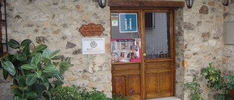 Un edificio de piedra con una puerta de madera, un letrero que dice 'Hostal Alba Tarutia', y un escalón que lleva a la entrada.