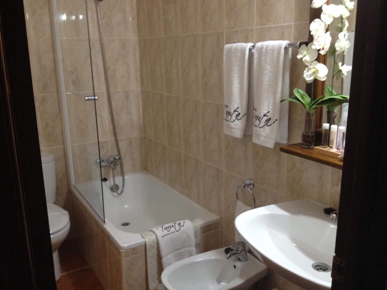 Een badkamer met een bad, een wastafel en een toilet. Handdoeken hangen aan de muur en er staat een plant op de plank.