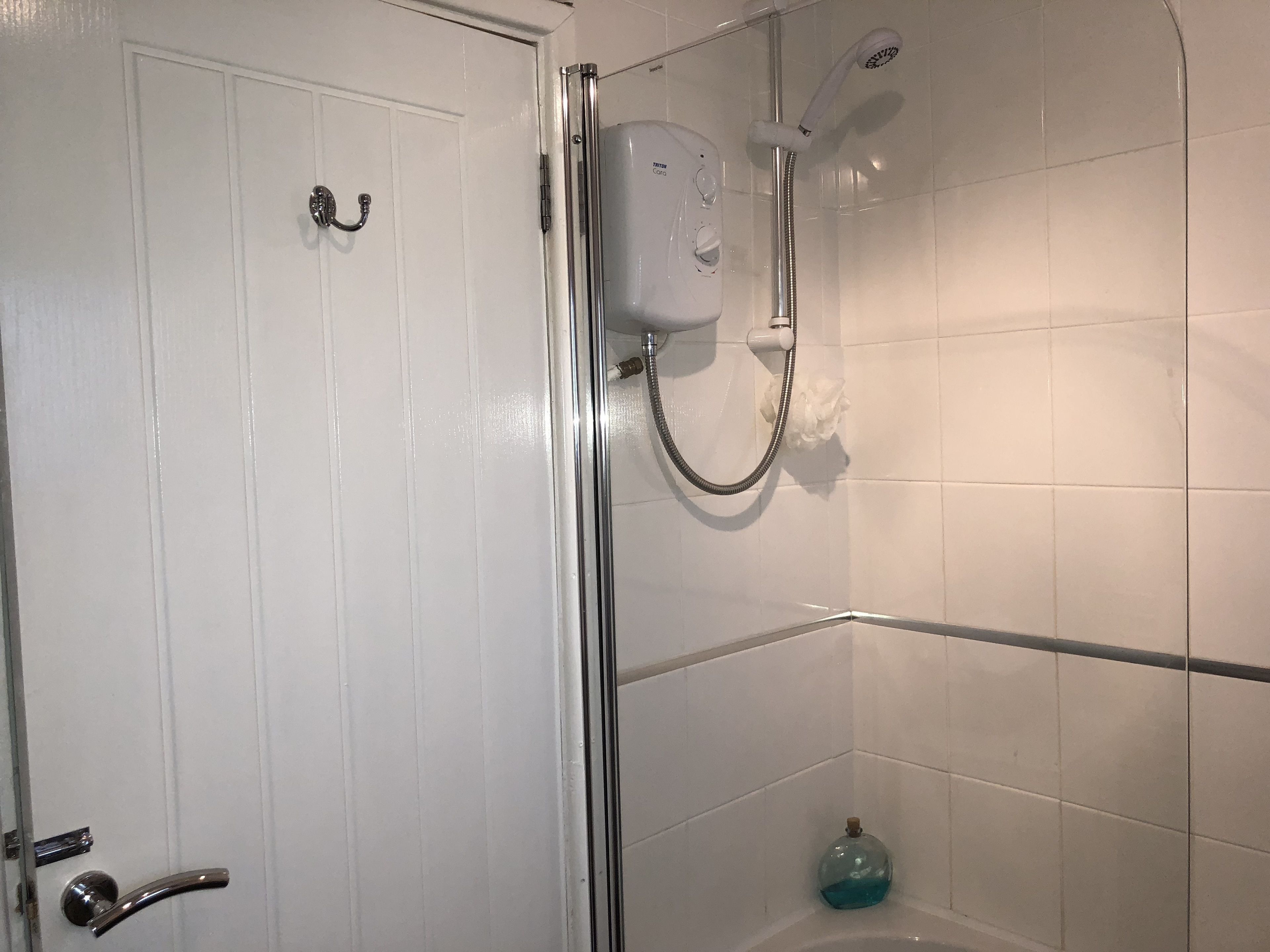 A bathroom with a white door, a shower with a handheld showerhead, and a soap dispenser.